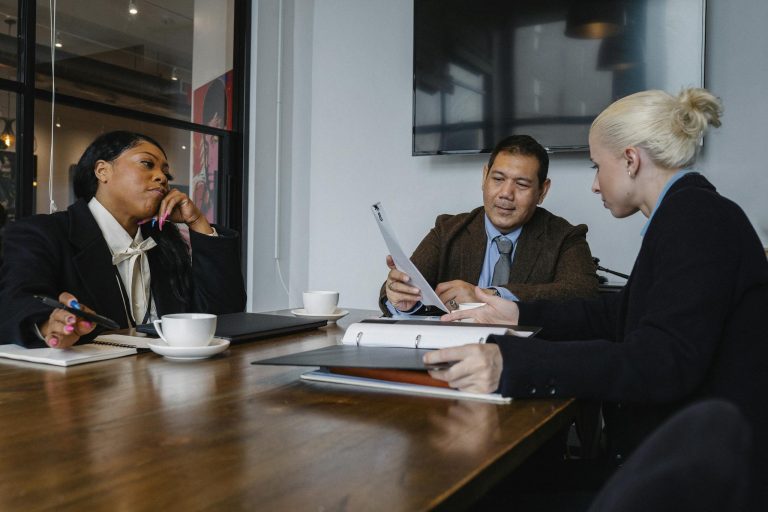 Multiethnic coworkers in formal wear sitting at table with documents and discussing details of business project